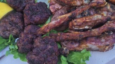 Platter of various types of meat including, pork, lamb, meatballs, and chicken served with lemon and tomato slices close-up top view.