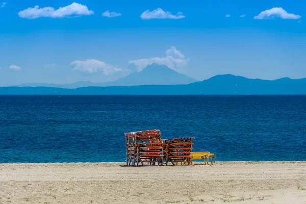 Stacked sea beds on an empty beach against blue sky. Day view of colourful sea beds on a sandy coast without crowd before a calm sea in Chalkidiki peninsula Greece, with background Mount Athos view.