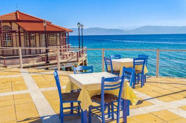 Yazın güneşli bir havada, tahta sandalyeleri ve masaları olan boş bir taverna restoranı..