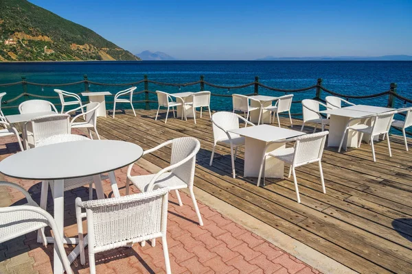 Yazın mavi gökyüzünün altında, deniz kenarında sandalyeleri ve masaları olan boş bir kafe..