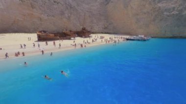 Zakynthos, Yunanistan - 10 Temmuz 2021: Navagio Plajı 'na deniz manzaralı tava, turistler ve İyon Adaları' nda demirlemiş turist gemileriyle kumlu sahilde çürüyen ünlü gemi enkazı.