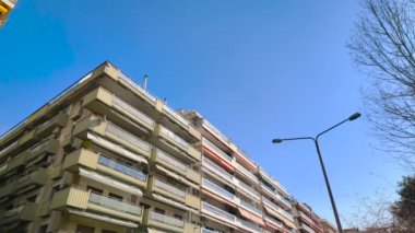 Yunanistan 'ın Selanik kentindeki Analipsi ilçesinde, açık mavi gökyüzü altında apartman blokları bulunan yoğun nüfuslu bir Avrupa kenti bölgesinin altında yürüyen POV görülüyor.