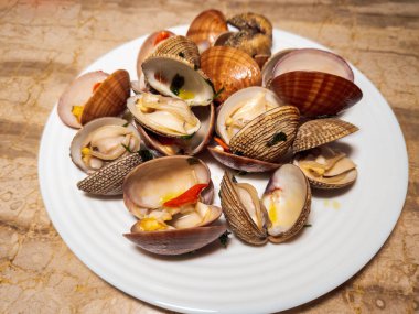 Taze pişmiş, kabuklu, açık Venüs istiridyeleri, yakın çekim beyaz tabak üzerinde servis edilir..