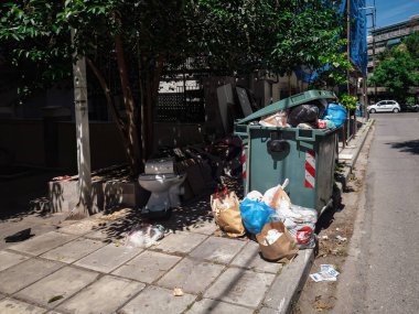 Selanik, Yunanistan - 7 Mayıs 2024: Tam teşekküllü bir çöp konteynırının önündeki kaldırımda çöpler.