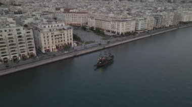 Selanik, Yunanistan - 30 Eylül 2020: Nikis Bulvarı boyunca deniz kenarı binaları ve Aristotelöz ana meydanı boyunca trafiği olan Thermaic Gulf 'ta seyreden teknenin akşam manzarası.