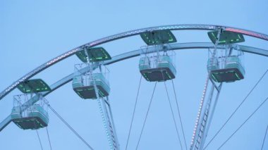 Büyük boş bir dönme dolap alacakaranlık gökyüzüne karşı duruyor. Parlak ışıkları lunaparkı aydınlatıyor..