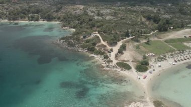 Yunanistan 'ın Chalkidiki kentindeki Akdeniz' deki sahil barına yeşil bitki örtüsü, kristal sular ve alçak katlı evlerle kayalık kıyı üzerinde gün uçuyor.