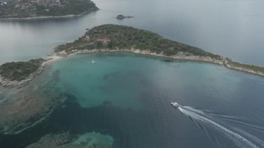 Yunanistan 'ın Chalkidiki yarımadasındaki Akdeniz' de yeşil plantasyonu olan ada girişinin yanındaki sakin sularda yelken açan küçük teknenin üzerinde uçmak.