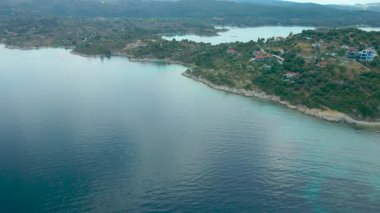 Yunanistan 'ın Chalkidiki Sithonia yarımadasında, Akdeniz' de düşük katlı evler ve yeşil bitki örtüsüyle denizden kıyıya uçma günü.