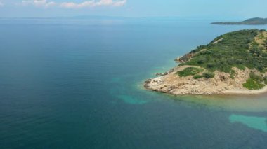 Yunanistan 'ın Chalkidiki yarımadasında Akdeniz' de mavi gökyüzüne karşı yeşil bitki örtüsüyle küçük ada şeridine yayılan gün.