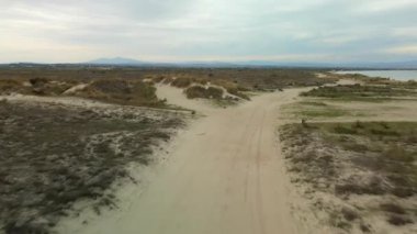 Boş toprak bir yol ve Yunanistan 'da bulutlu bir gökyüzünün altında deniz kenarında kumlu yolları olan geniş bir çöl manzarası üzerinde gündüz görüşü.