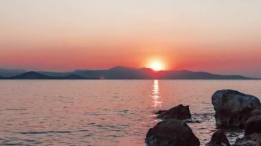 Beach sunset time lapse with orange sky and sun setting behind mountains.