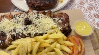 Kızarmış peynirle kaplı sulu ızgara tavuğun yanında kızarmış patates ve taze domates dilimleri ve yanında paprika soslu Yunan köftesi köftesi..