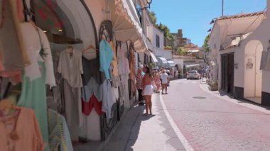 Positano, İtalya - 15 Haziran 2024: Ziyaretçiler Positano 'da büyüleyici caddelerde gezinirken, parlak Akdeniz güneşi altındaki ana yol üzerindeki dükkanlar.