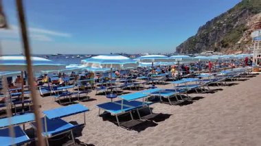 Positano, İtalya - 15 Haziran 2024: Ziyaretçiler Amalfi Sahili 'nde güneşli bir günün keyfini çıkarıyorlar, etrafları parlak şemsiyeler ve kayalık kayalıklarla çevrili. 