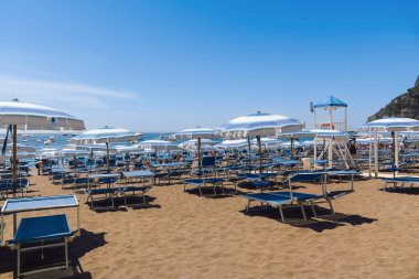 Positano, İtalya - 15 Haziran 2024: güneş şemsiyeleri ve şezlonglar Amalfi Sahili 'ndeki kumlu plajda yüzerken, tekneler berrak bir gökyüzünün altında parlak mavi sularda sürükleniyorlar..