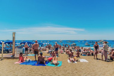 Positano, İtalya - 15 Haziran 2024: Kalabalık Amalfi Sahili 'nin kumlu sahilinde sıcak güneşin keyfini çıkarıyor, tekneler açık mavi suyu mükemmel bir günde noktalıyor..