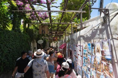 Positano, İtalya - 15 Haziran 2024: Ziyaretçiler yerel sanat ve çiçeklerle süslenmiş canlı bir patikada geziniyorlar. Atmosfer Amalfi Sahili 'nin özünü yakalıyor..