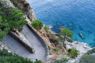 Discover the breathtaking trail of historic Vi Krupp along the cliffs of Capri Island, Italy surrounded by lush greenery and crystal-clear blue waters.