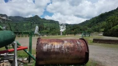 Ormanın ortasındaki bir volkanda termik santral, büyük borulardan yükselen buhar, dönen türbinler, tropikal adalar, dağlar, drone çekimleri.
