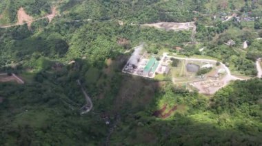 Ormanın ortasındaki bir volkanda termik santral, büyük borulardan yükselen buhar, dönen türbinler, tropikal adalar, dağlar, drone çekimleri.