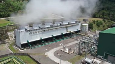 Ormanın ortasındaki bir volkanda termik santral, büyük borulardan yükselen buhar, dönen türbinler, tropikal adalar, dağlar, drone çekimleri.