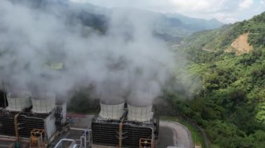 Ormanın ortasındaki bir volkanda termik santral, büyük borulardan yükselen buhar, dönen türbinler, tropikal adalar, dağlar, drone çekimleri.