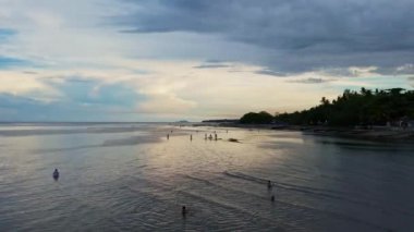 İnsanlar tropikal bir adada deniz mahsulleri topluyor, günbatımı, güneş dağın arkasına gidiyor, balıkçı tekneleri, tropikal bir adada okyanus akıntısı. Yüksek kalite 4k görüntü