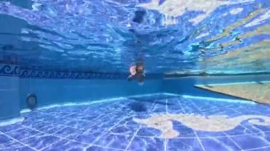 Küçük kızlar, kız kardeşler, üçüzler bir havuzda maske takıp suyun altında şnorkelle yüzerler. 3 yaşındaki yüksek kaliteli 4k 'lık üçlü kız kardeşler.