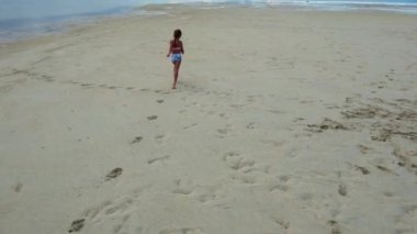Beyaz kum tükürüğü, balık sürüsü, kumda koşan kız, okyanusun izlerini bırakıyor. Mayoyla kumda koşan küçük bir kız. Yüksek kalite 4k görüntü