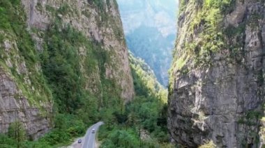 Yazın dar bir dağ geçidi, bir dron geçitten uçuyor, duvarlar yüksek ve taştan, yeşil ağaçlar yetişiyor, gökyüzü bulutsuz, güneş parlak. Yüksek kalite 4k görüntü