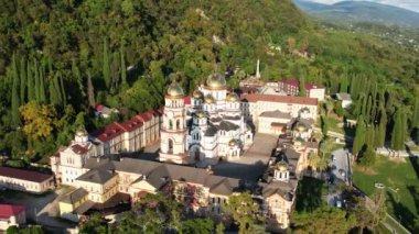 Abhazya 'daki yeni Athos Manastırı, Yeni Athos şehri, İHA görüntüleri, sonbahar yeşil tepeleri ve mavi deniz, batan güneşte parıldayan kiliselerin altın kubbeleri, Ortodoks haçları, selvi ağaçları ve palmiye ağaçları.