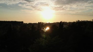 Batan güneş göle yansıyor, sarı günbatımı küçük bir köyün bacalarından siyah bir duman çıkarıyor. Güneş yavaşça deniz ufkuna düşüyor. Yüksek kalite 4k görüntü