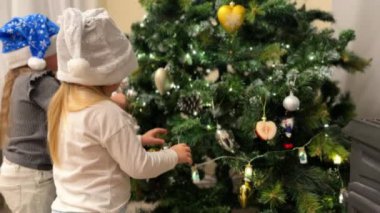 Üçüzlerin üç kız kardeşi Noel ağacını oyuncaklar ve çelenklerle süslüyor çocuklar renkli Noel Baba şapkaları takıyor Noel ağacının yanında bir şömine yanıyor.. 