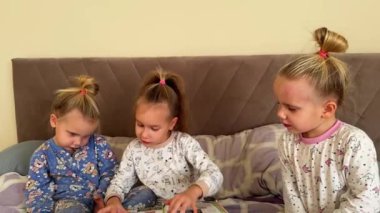 Küçük kız kardeşler yatakta otururken birlikte kitap okurlar. Pijama giyiyorlar. Yüksek kalite 4k görüntü