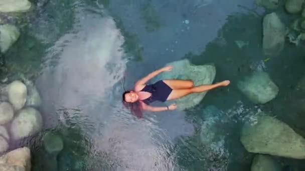 热带岛屿上的一条山河上 一个身着黑色泳衣的无人驾驶女孩拍摄了一个火山泉的蓝色热水 高质量的4K镜头 — 图库视频影像