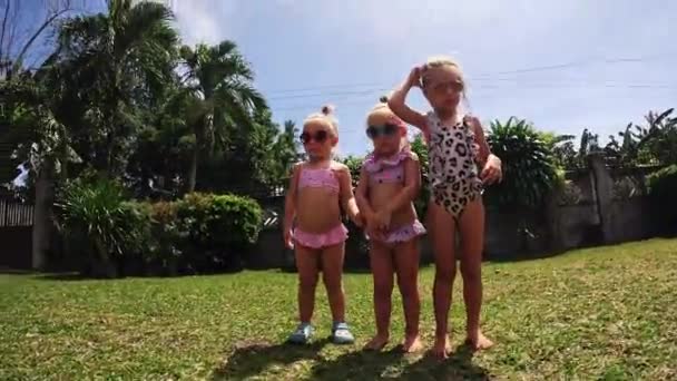 三胞胎跳在草地上 小女孩 三个戴着太阳镜的姐姐 — 图库视频影像