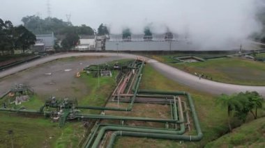 Ormanın ortasındaki bir volkanda termik santral, büyük borulardan yükselen buhar, dönen türbinler, tropikal adalar, dağlar, drone çekimleri.