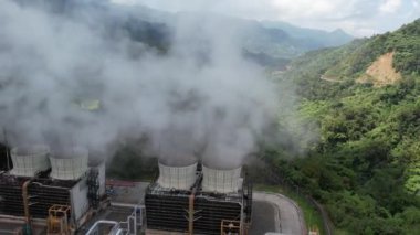 Ormanın ortasındaki bir volkanda termik santral, büyük borulardan yükselen buhar, dönen türbinler, tropikal adalar, dağlar, drone çekimleri.