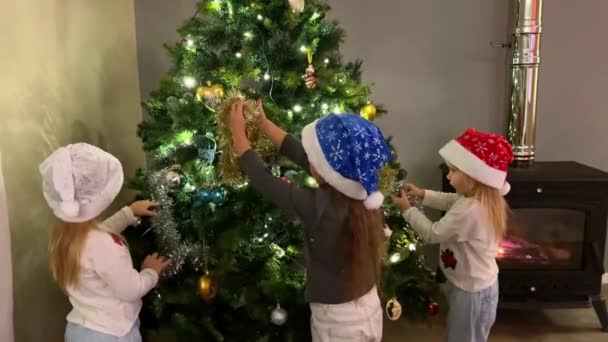 Drei Kleine Drillingsschwestern Schmücken Den Weihnachtsbaum Mit Spielzeug Und Girlanden — Stockvideo