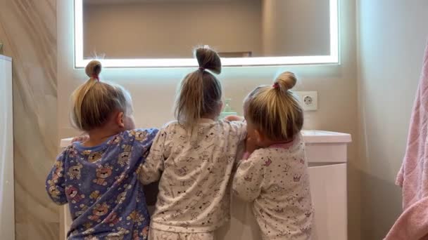小さな姉妹は 鏡の前にトイレで歯を磨く双子を三つに分け さまざまな色のパジャマ 歯ブラシを着ています 高品質の4K映像 — ストック動画