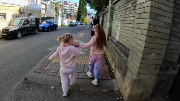 Dwie Siostry Bliźniaczki Chodzą Chodnikiem Trzymając Się Ręce Ulica Miasta — Wideo stockowe