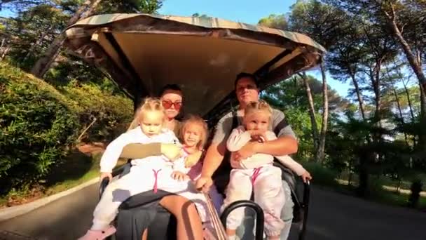 一个有三个孩子的家庭在公园里坐着一辆高尔夫球车 三胞胎妹妹 爸爸妈妈 当你开车时 相机从后面拍摄 高质量的4K镜头 — 图库视频影像
