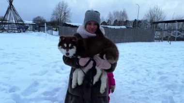 Anne ve üçüzlerin kızı kışın kahverengi köpek yavrusuyla yürüyor, anne kucağında köpek yavrusuyla. Yüksek kalite 4K görüntü. Yüksek kalite 4k görüntü