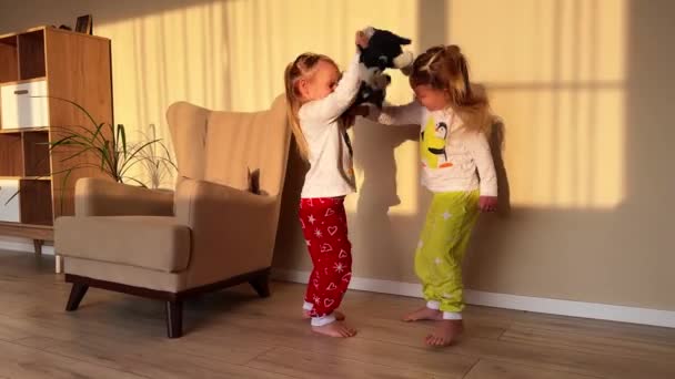 小さな双子の姉妹が部屋にぬいぐるみの犬を引っ張っている 高品質の4K映像 — ストック動画