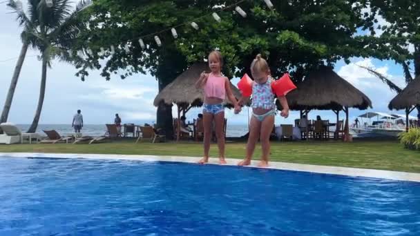 身穿泳衣的孪生姐妹跳入热带岛屿沿岸的蓝色水池 孩子们戴着臂章 阳光灿烂的一天 高质量的4K镜头 — 图库视频影像