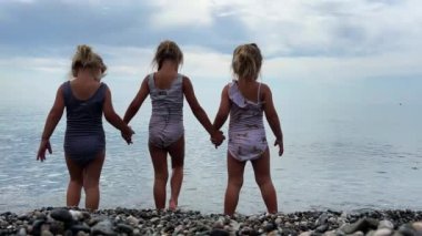 Triplet kardeşler çakıl taşı sahilinde deniz suyunda yüzer, çam ağaçları arkada görülebilir. Yüksek kalite 4k görüntü