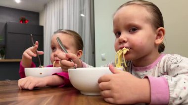 İki ikiz kardeş masada otururken beyaz tabaktan spagetti yiyorlar. Yüksek kalite 4k görüntü