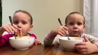 İki ikiz kardeş masada otururken beyaz tabaktan spagetti yiyorlar. Yüksek kalite 4k görüntü