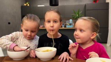 Üç küçük üçüz kız kardeş mutfakta beyaz tabaklardan spagetti yiyorlar. Yüksek kalite 4k görüntü